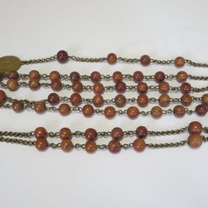 May include: A vintage rosary with multiple strands of brown wooden beads. The beads are connected by a silver-colored chain. A small, round, gold-colored medallion is visible at the top.