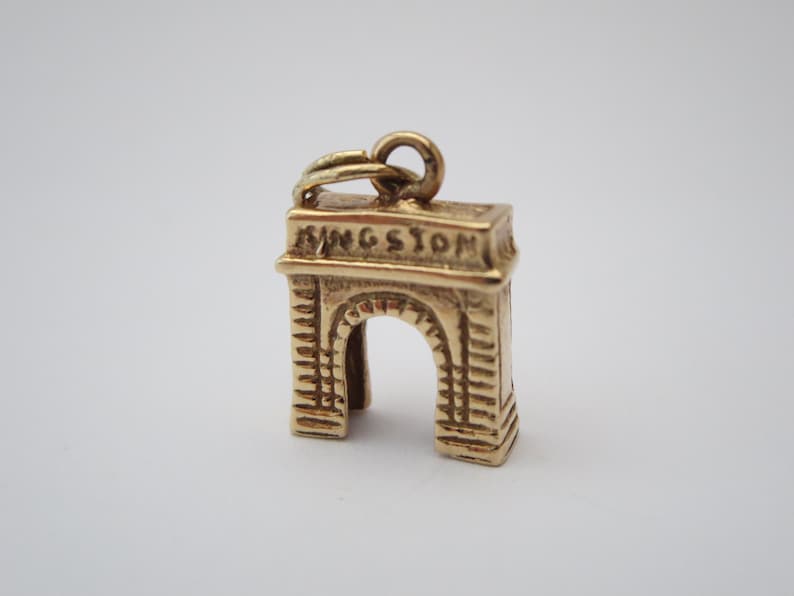 Puede incluir: Encanto de oro en forma de arco de Kingston, Nueva York. El encanto tiene la palabra "Kingston" inscrita en la parte superior.