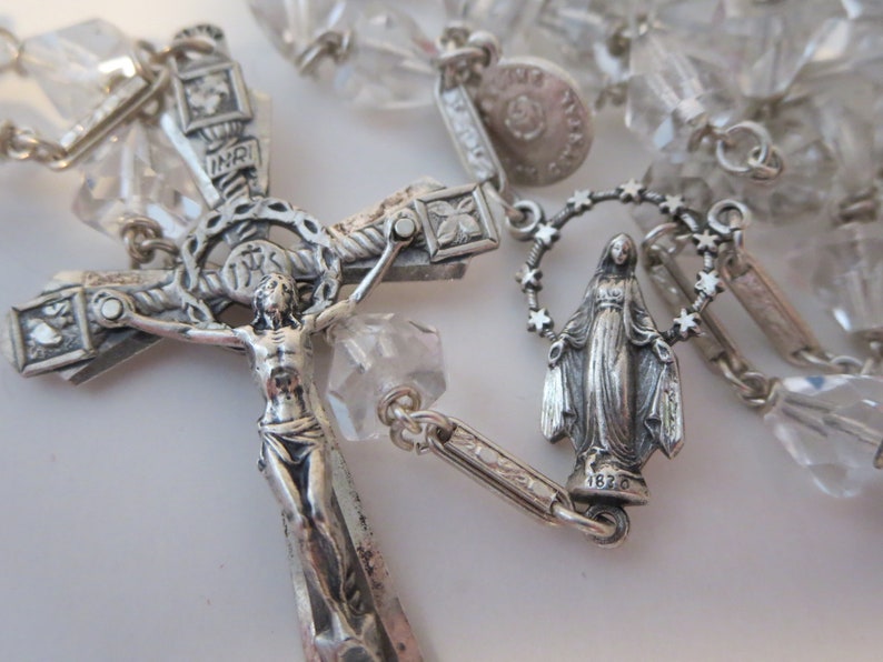 Op de afbeelding: Een zilveren rozenkrans met kristallen kralen. Het middelpunt is een kruisbeeld met een figuur van Jezus Christus en een zilveren hanger van de Maagd Maria.