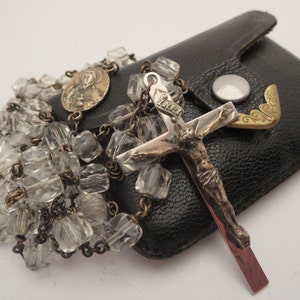 May include: A clear glass crystal rosary with a silver and gold crucifix and a small round medal. The rosary is in a black leather case.