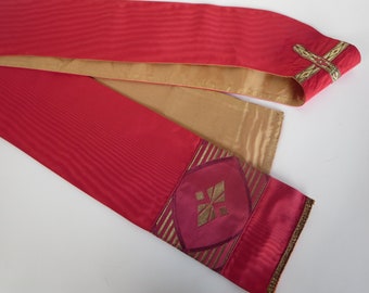 May include: A red and gold liturgical stole with a burgundy cross design. The stole is trimmed with gold braid and has a gold cross on the end.