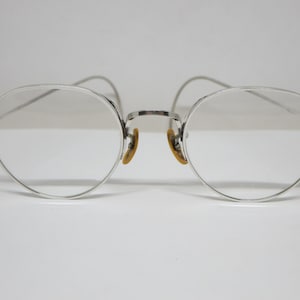 May include: Silver-rimmed round eyeglasses with clear lenses.