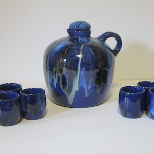 May include: A set of blue and white ceramic serving pieces, including a pitcher and six small cups. The pitcher has a lid and a handle. The cups are all the same size and shape. The pieces are decorated with a blue and white glaze.