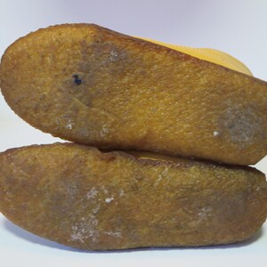 May include: Close-up of the soles of two yellow suede shoes stacked. The soles are textured, light brown rubber with white marks. The shoes appear new. The image shows the underside of the shoes.