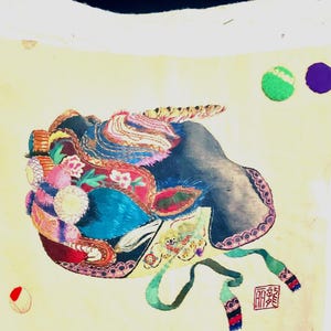 May include: A decorative pillow with a colorful abstract design. The artwork features a mix of blues, pinks, greens, and yellows, with a touch of red. The pillow has a white border and a light yellow center.