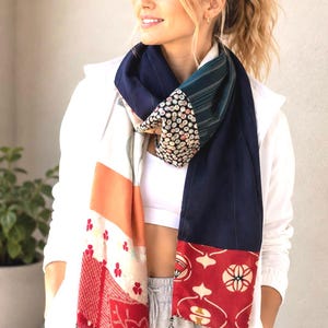 May include: A long rectangular scarf featuring a patchwork design of various fabrics. The scarf includes sections of solid navy blue, a red panel with cream-colored circular patterns, a white section with small red floral motifs, and a dark patterned section.