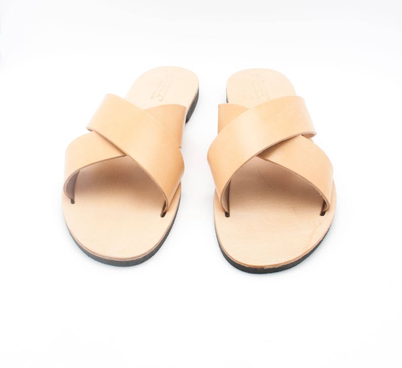 K&ouml;nnte beinhalten: Ein Paar hellbraune Ledersandalen mit gekreuzten Riemen. Die Sandalen haben einen schlichten, minimalistischen Stil mit schwarzer Sohle. Die Sandalen sind f&uuml;r den l&auml;ssigen Gebrauch konzipiert.
