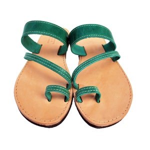 Puede incluir: Un par de sandalias de cuero hechas a mano. Las sandalias presentan una plantilla marr&oacute;n claro con un dise&ntilde;o de correas de cuero verde oscuro. Las correas est&aacute;n cosidas con hilo blanco. Las sandalias tienen una presilla para el dedo gordo y una correa que rodea el tobillo.