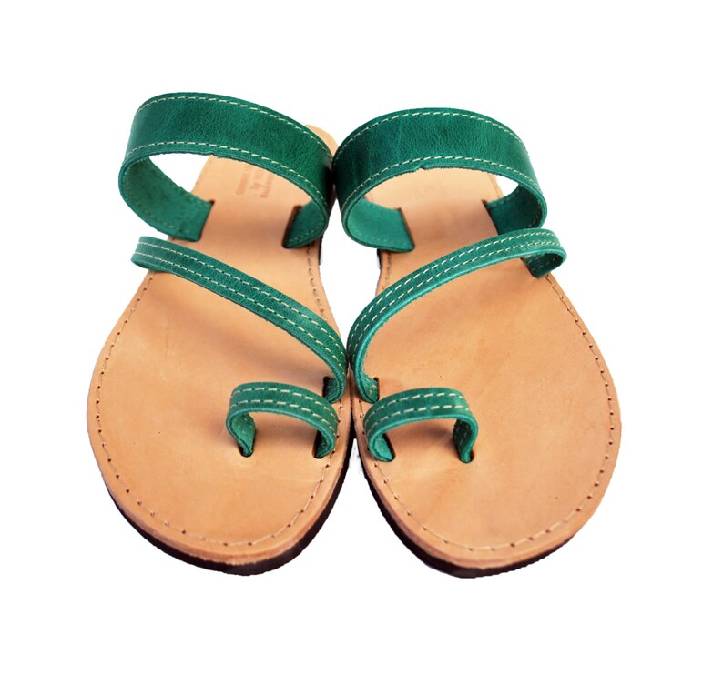Puede incluir: Un par de sandalias de cuero hechas a mano. Las sandalias presentan una plantilla marr&oacute;n claro con un dise&ntilde;o de correas de cuero verde oscuro. Las correas est&aacute;n cosidas con hilo blanco. Las sandalias tienen una presilla para el dedo gordo y una correa que rodea el tobillo.