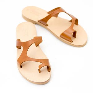 May include: A pair of brown leather sandals with a toe ring and criss-cross straps.
