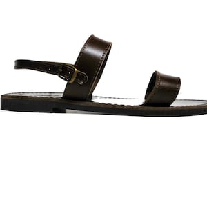 May include: A single brown leather sandal with a buckle closure. The sandal features a strap that goes around the ankle and a strap over the toes. The sole is dark brown.