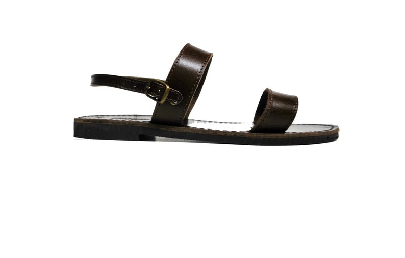 May include: A single brown leather sandal with a buckle closure. The sandal features a strap that goes around the ankle and a strap over the toes. The sole is dark brown.