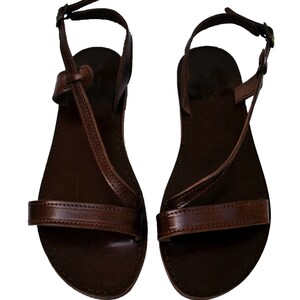 May include: A pair of brown leather sandals with a simple design. The sandals have a strap that goes around the ankle and a strap across the toes. The sandals are made of a smooth, shiny leather.