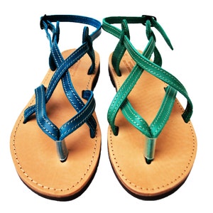 May include: A pair of leather sandals with blue and green straps. The sandals have a thong-style design with a light brown sole and a silver-colored toe post. The straps are stitched with white thread and have adjustable buckles.