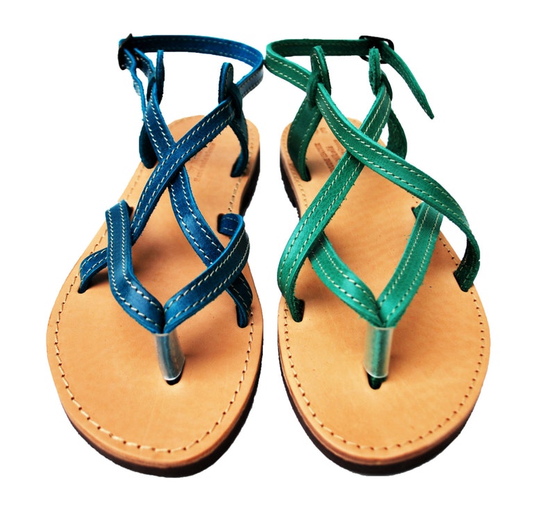 May include: A pair of leather sandals with blue and green straps. The sandals have a thong-style design with a light brown sole and a silver-colored toe post. The straps are stitched with white thread and have adjustable buckles.