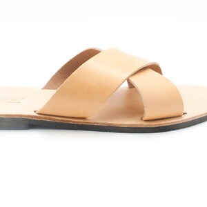K&ouml;nnte beinhalten: Ein Paar hellbraune Ledersandalen mit einem Kreuzriemen-Design. Die Sandalen haben eine nat&uuml;rliche Lederfarbe und eine schwarze Sohle. Das Design ist schlicht und minimalistisch, geeignet f&uuml;r Freizeitkleidung.