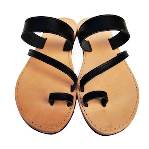 Puede incluir: Un par de sandalias de cuero con suela marr&oacute;n claro y correas negras. Las sandalias tienen una presilla para el dedo gordo y una correa en el tobillo. Sandalias dise&ntilde;adas para la comodidad y el estilo.