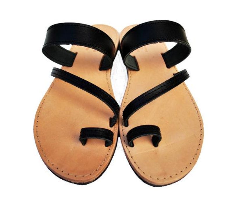 Puede incluir: Un par de sandalias de cuero con suela marr&oacute;n claro y correas negras. Las sandalias tienen una presilla para el dedo gordo y una correa en el tobillo. Sandalias dise&ntilde;adas para la comodidad y el estilo.