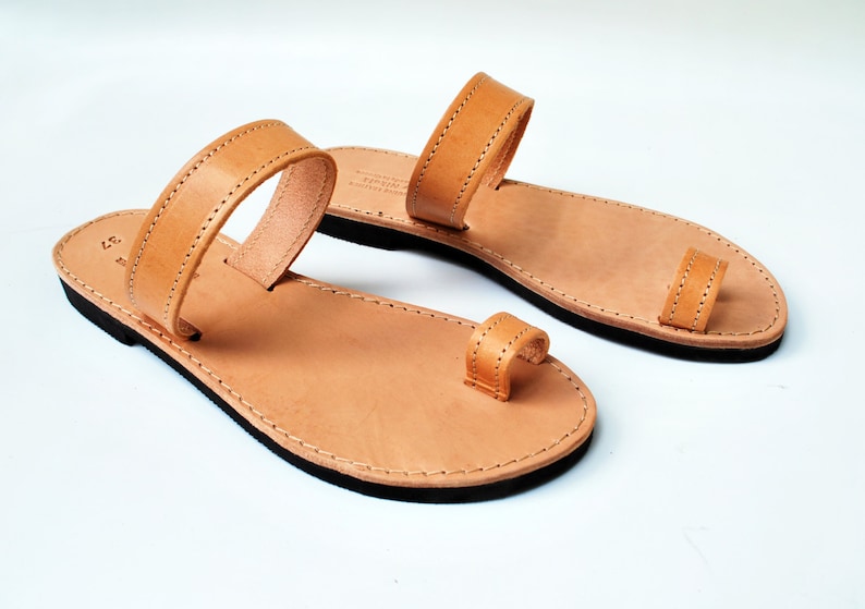Peut inclure: Paire de sandales en cuir marron clair avec une boucle d'orteil et une bride sur le dessus du pied. Les sandales ont une semelle noire et sont pr&eacute;sent&eacute;es sur fond blanc. Taille 37 (environ 23,5 cm).