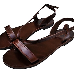 May include: A pair of brown leather sandals with thin straps and adjustable buckles. The sandals have a simple design with a flat sole, suitable for casual wear. The leather appears to be smooth and well-crafted.