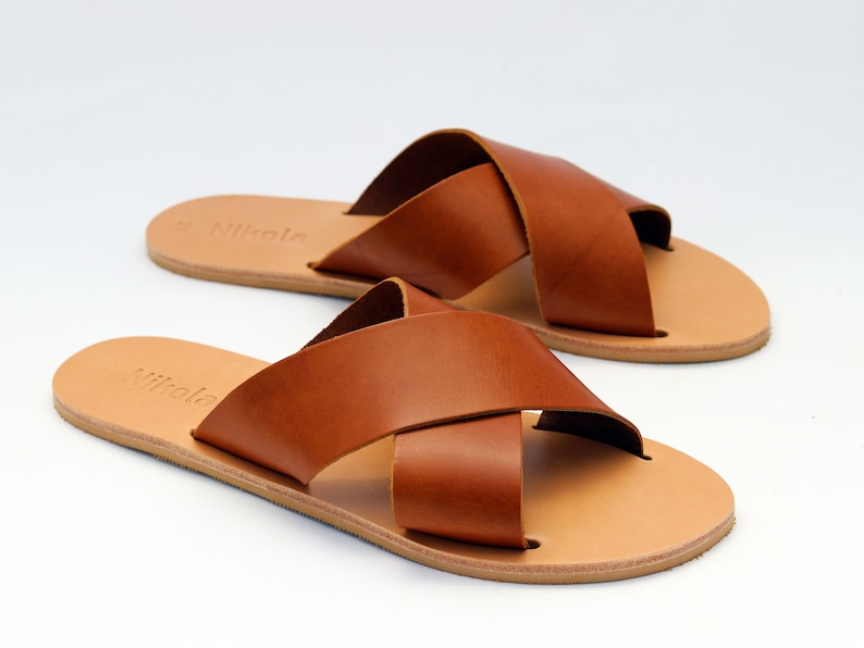 Peut inclure: Une paire de sandales en cuir marron avec un design &agrave; lani&egrave;res crois&eacute;es. Les sandales ont une semelle marron clair et le mot "Nikola" est imprim&eacute; sur la semelle int&eacute;rieure. Les sandales sont pr&eacute;sent&eacute;es sur fond blanc.