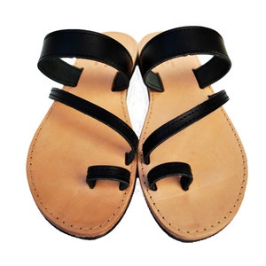 May include: A pair of black leather sandals with a light brown footbed. The sandals feature a toe loop and straps that cross over the foot. The sole is stitched around the edges. These sandals are suitable for casual wear.