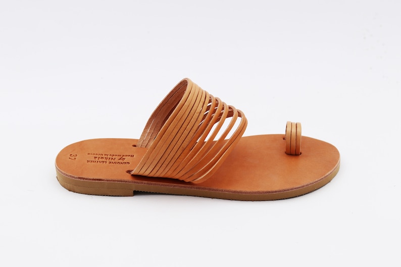 May include: A pair of light brown leather sandals with a toe loop and multiple straps across the top. The sandals are made of genuine leather and are size 37. The sole is a darker brown color.
