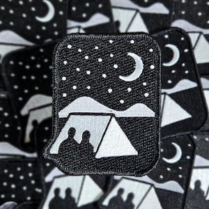 May include: Black patch depicting a camping scene under a starry night sky. The design includes a white tent with two silhouetted figures, a crescent moon, and a mountain range. The patch is surrounded by other similar patches.