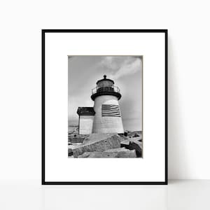 Puede incluir: Una fotografía en blanco y negro de un faro con una bandera estadounidense en el lateral. El faro se encuentra en una costa rocosa.