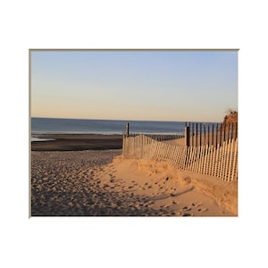 Puede incluir: Una valla de madera conduce a una playa de arena con huellas y una vista del océano en la distancia.