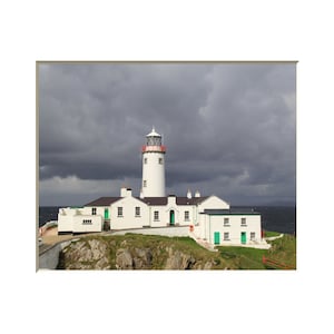 Puede incluir: Un faro blanco con techo rojo se alza sobre un acantilado rocoso con vistas al océano. El cielo está cubierto de nubes oscuras.