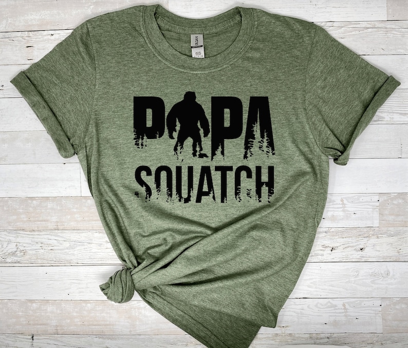 May include: Green t-shirt with a black graphic of a Bigfoot silhouette and the text "DAPA SQUATCH".