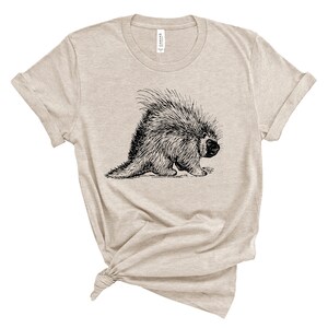 K&ouml;nnte beinhalten: Ein beiges T-Shirt mit einer Schwarzwei&szlig;illustration eines Stachelschweins.