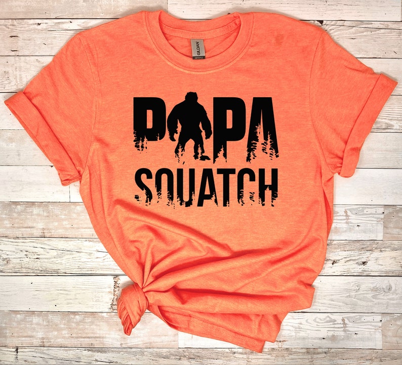May include: Orange t-shirt with a black graphic of a Bigfoot with the text "DAPA SQUATCH" printed on it.