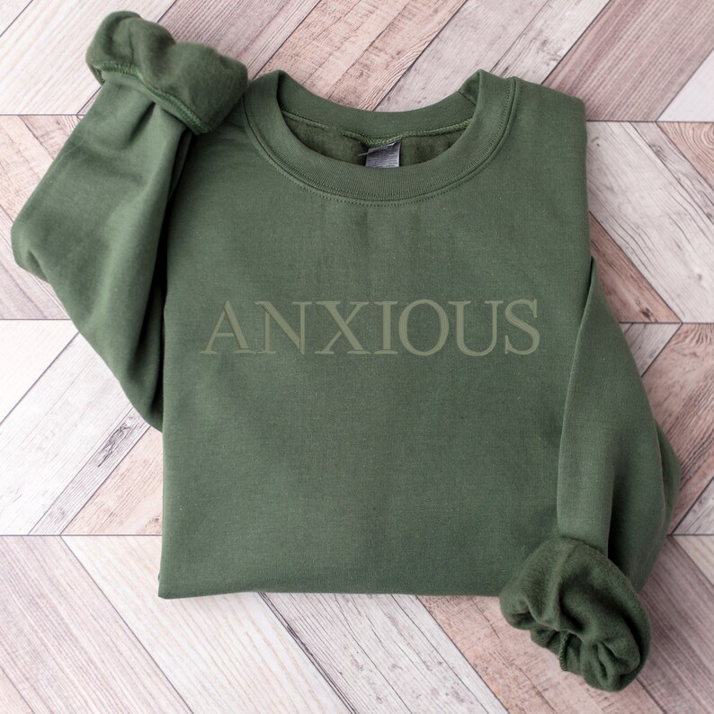 May include: A green sweatshirt with the word "ANXIOUS" printed in white on the front.