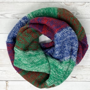 May include: A green, blue, and red striped infinity scarf. The scarf is made of a soft, knitted fabric.