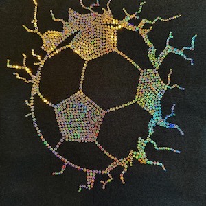 Peut inclure: Tissu noir avec un motif de ballon de football composé de strass irisés. Le ballon est souligné de strass et présente un effet fissuré, créant un design étincelant et accrocheur.