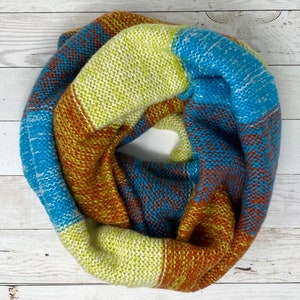Puede incluir: Una bufanda de punto infinito de colores con rayas azules, amarillas y marrones.