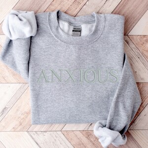 May include: Gray sweatshirt with the word "ANXIOUS" printed in green on the front.