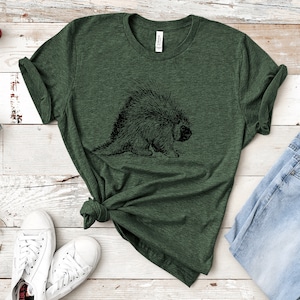 K&ouml;nnte beinhalten: Ein gr&uuml;nes T-Shirt mit einer schwarz-wei&szlig;en Illustration eines Stachelschweins auf der Vorderseite.
