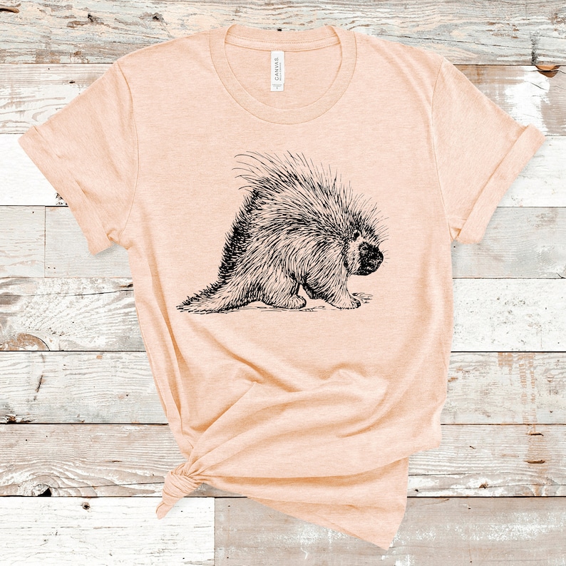 K&ouml;nnte beinhalten: Ein helles, pfirsichfarbenes T-Shirt mit einer Schwarz-Wei&szlig;-Zeichnung eines Stachelschweins auf der Vorderseite.