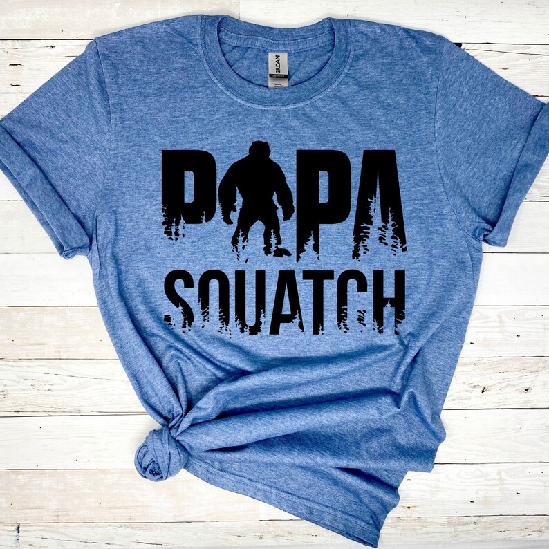May include: A blue t-shirt with a black graphic print of a Bigfoot figure and the text "Papa Squatch".