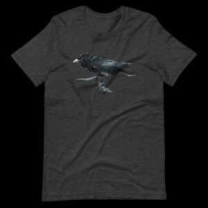 Puede incluir: Una camiseta gris oscuro jaspeada con una ilustraci&oacute;n de cuervo negro. El cuervo est&aacute; posado en una rama y tiene las alas extendidas.