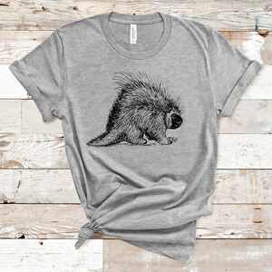 K&ouml;nnte beinhalten: Ein graues T-Shirt mit einer schwarz-wei&szlig;en Illustration eines Stachelschweins auf der Vorderseite.
