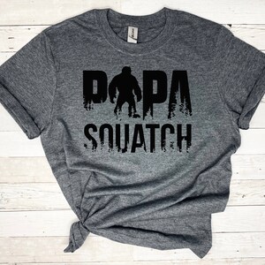 May include: Gray t-shirt with a black graphic of a Bigfoot with the text "Papa Squatch" printed on it.