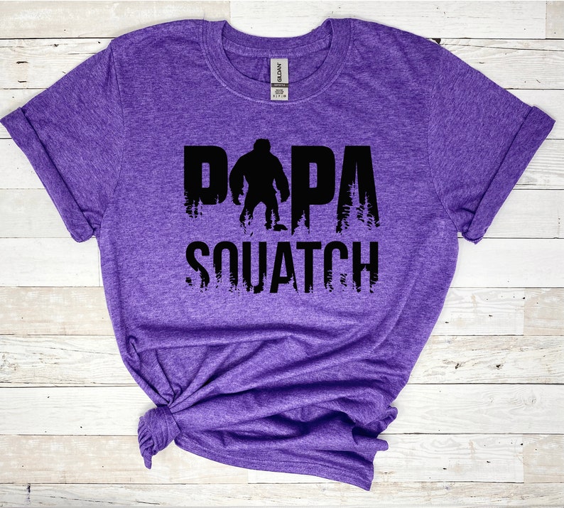 May include: Purple t-shirt with a black graphic of a Bigfoot with the text "Papa Squatch".