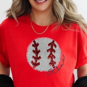 Op de afbeelding: Rood T-shirt met een baseball-ontwerp van pailletten en de naam "Ethan" eronder.
