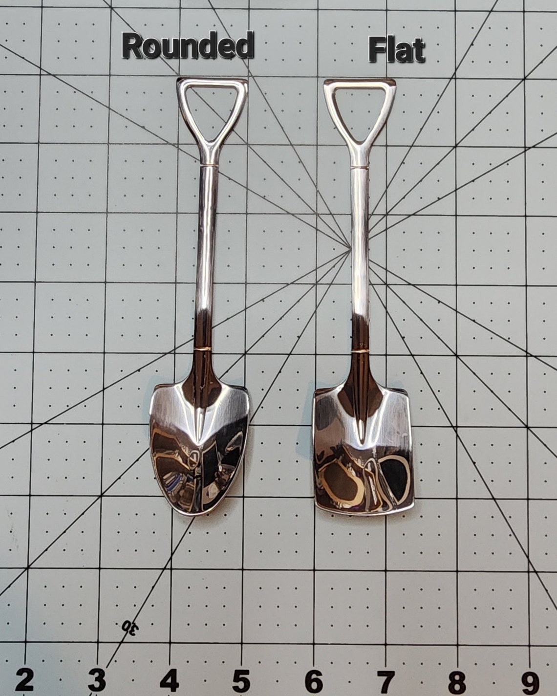 May include: Two silver miniature shovels, one with a rounded edge and one with a flat edge. The shovels are labeled 'Rounded' and 'Flat'.