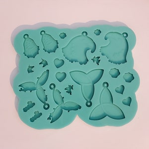 Puede incluir: Un molde de silicona turquesa con varias formas para hacer joyas, incluyendo corazones, estrellas y una cola de sirena.