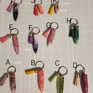 May include: Ten keychains with different colored tassels and glitter filled bullet casings. The keychains are labeled A through K.